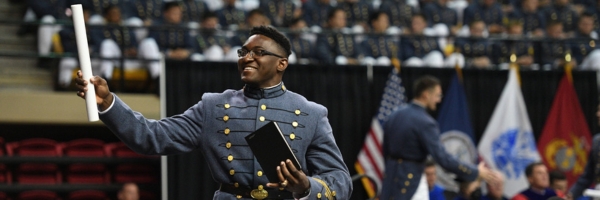 Cadet raises diploma towards a cheering crowd in Cameron Hall at VMI during Commencement.